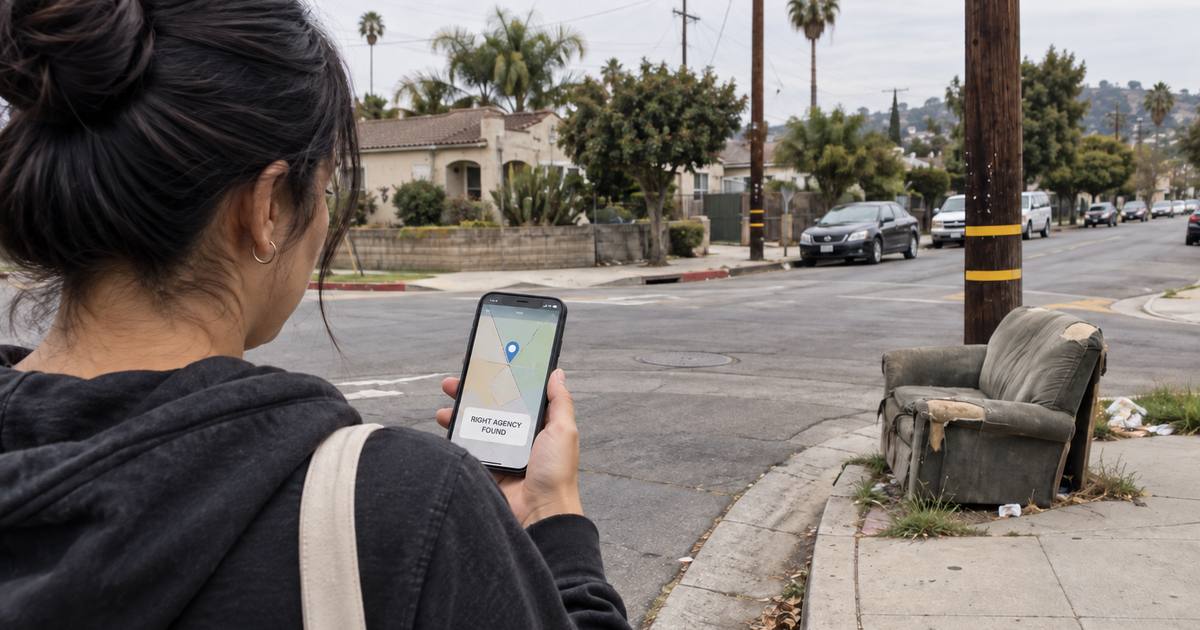 A resident on a Los Angeles corner holding a phone that reads Right Agency Found, beside a couch dumped on the sidewalk