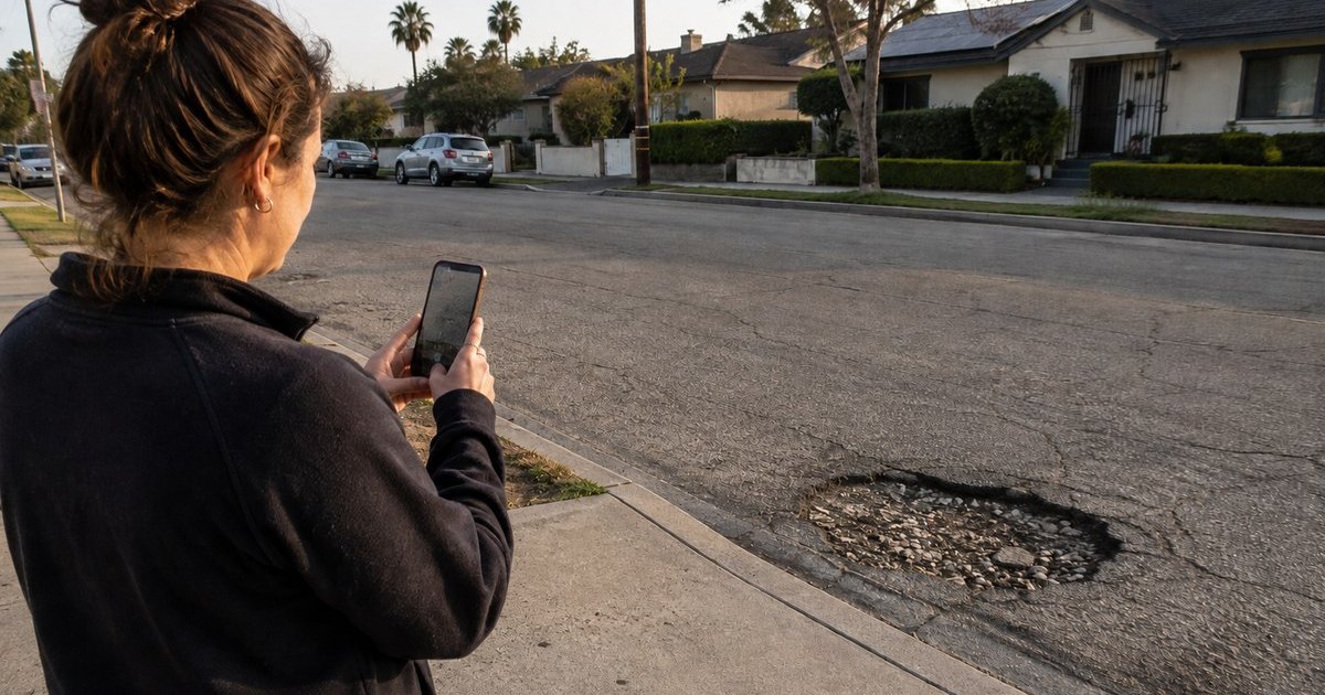 A resident photographing a pothole on a residential Los Angeles street